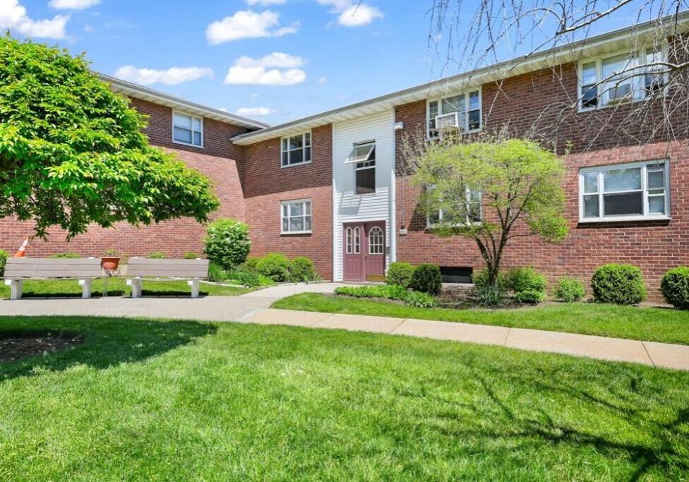 A brick apartment building with green lawns and trees.
