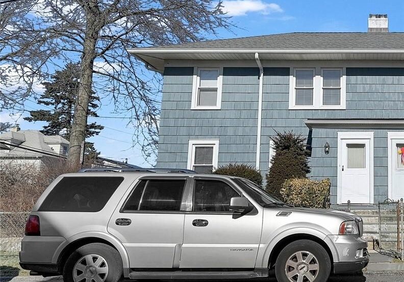 Silver SUV parked in front of a two-story blue house on a sunny day.