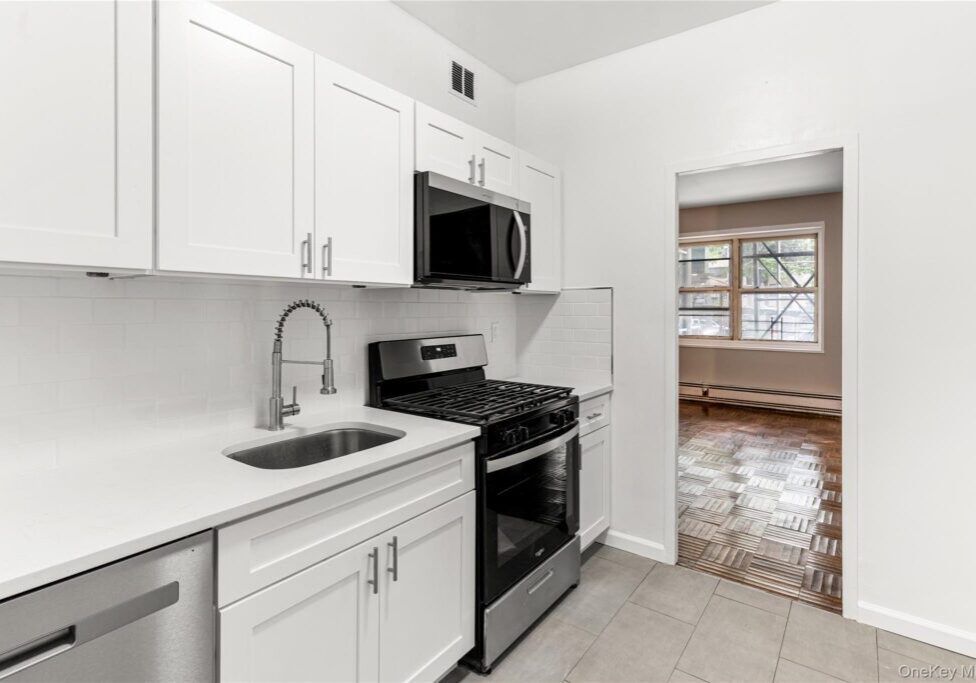 Modern kitchen with white cabinets and black appliances.