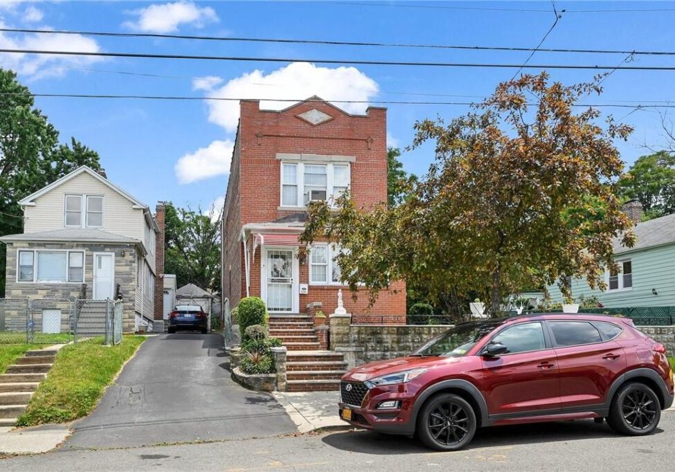 A brick two-story house with stairs and a red car parked in front.