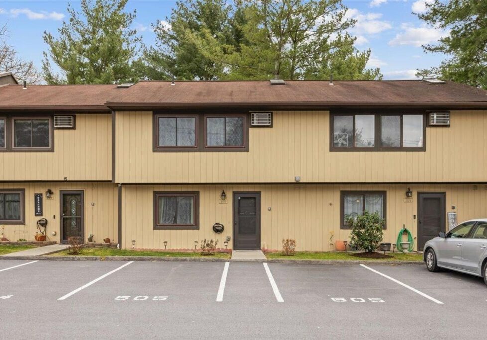 Two-story townhouse with beige siding and marked parking spaces in front.