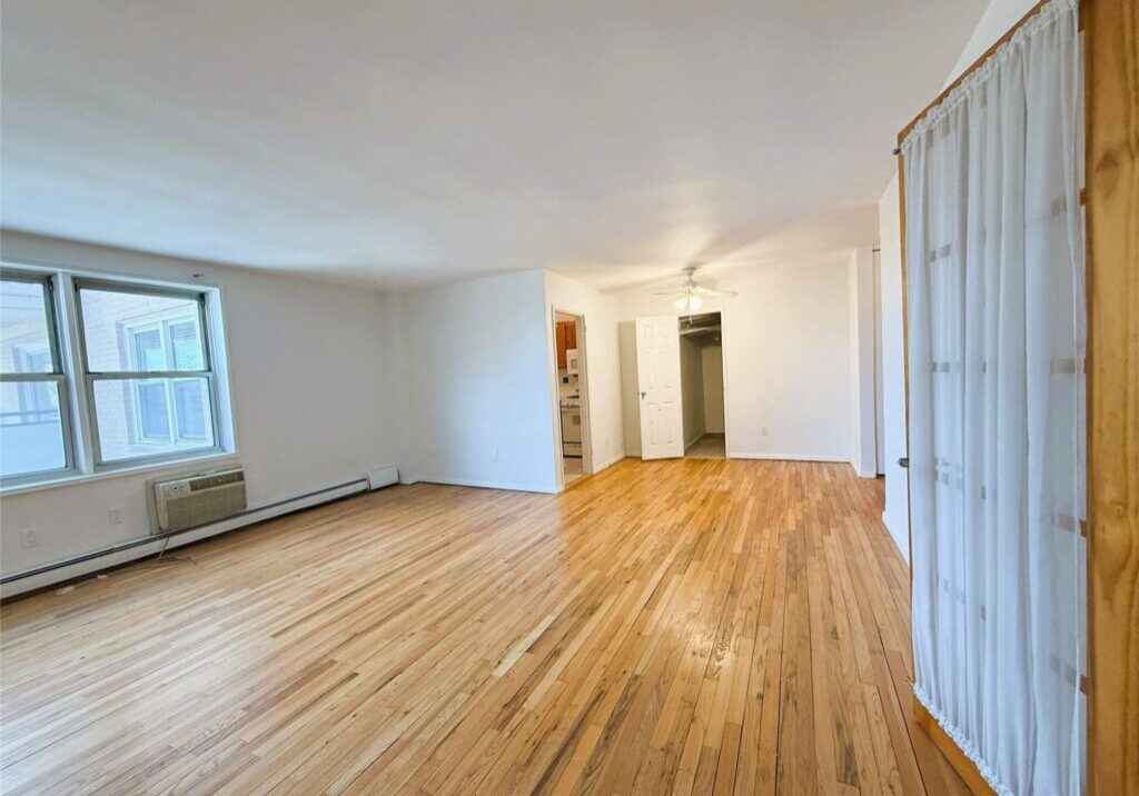 Empty room with wooden flooring and white walls.