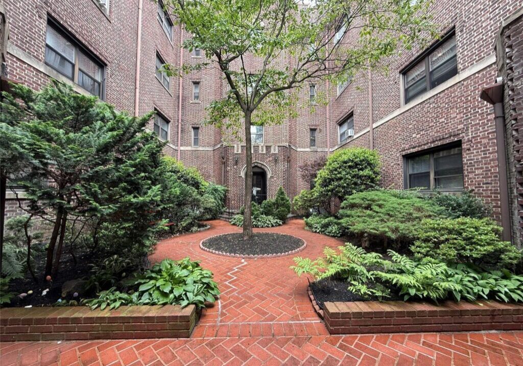Cozy outdoor courtyard with brick flooring and lush greenery surrounded by brick buildings.