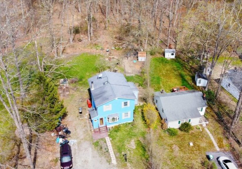 Aerial view of a blue house surrounded by trees and vehicles.