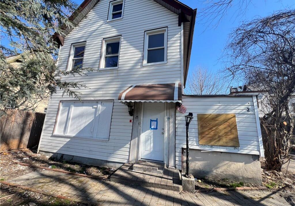 Old white house with boarded windows and a clear blue sky.