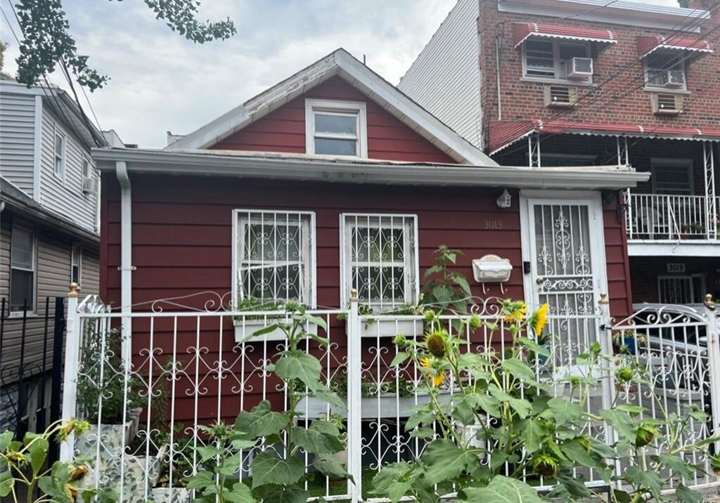 Cozy red house with white trim and lush green plants in front.