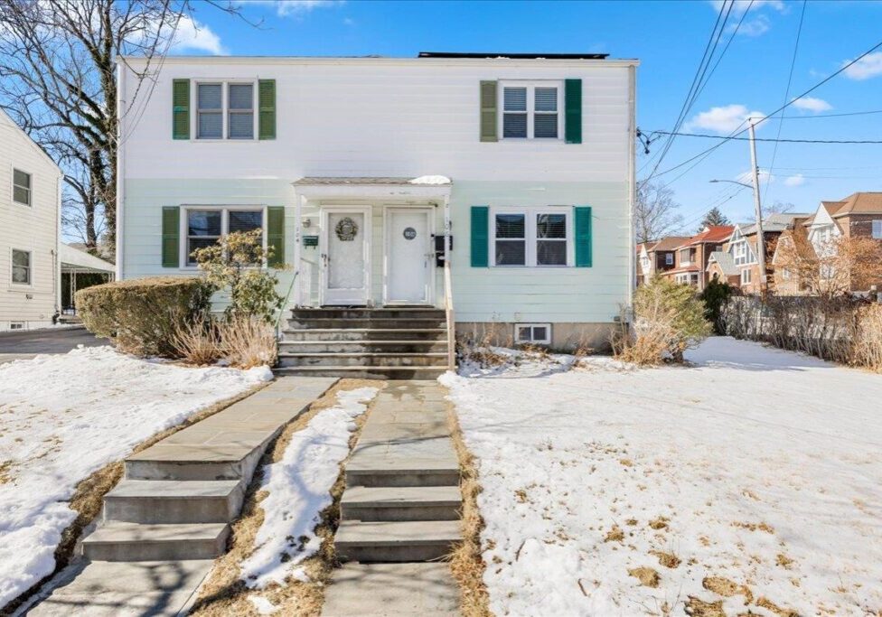 Two-story white house with snow-covered yard and front stairs.