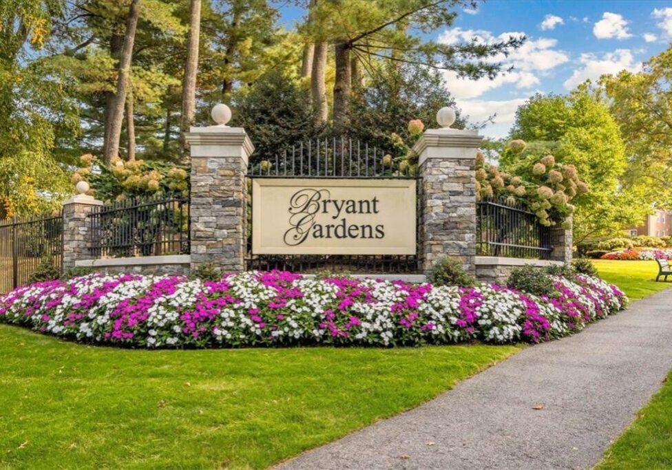 Entrance sign to Bryant Gardens surrounded by flowers and greenery.