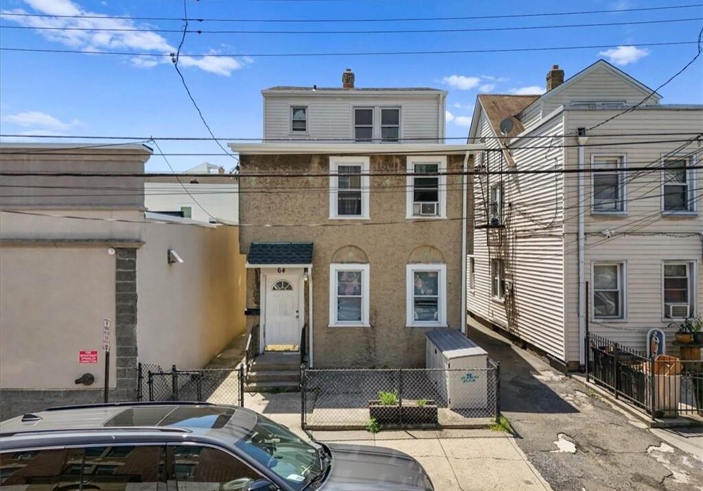 Three-story brick townhouse in a residential area with cars parked outside.