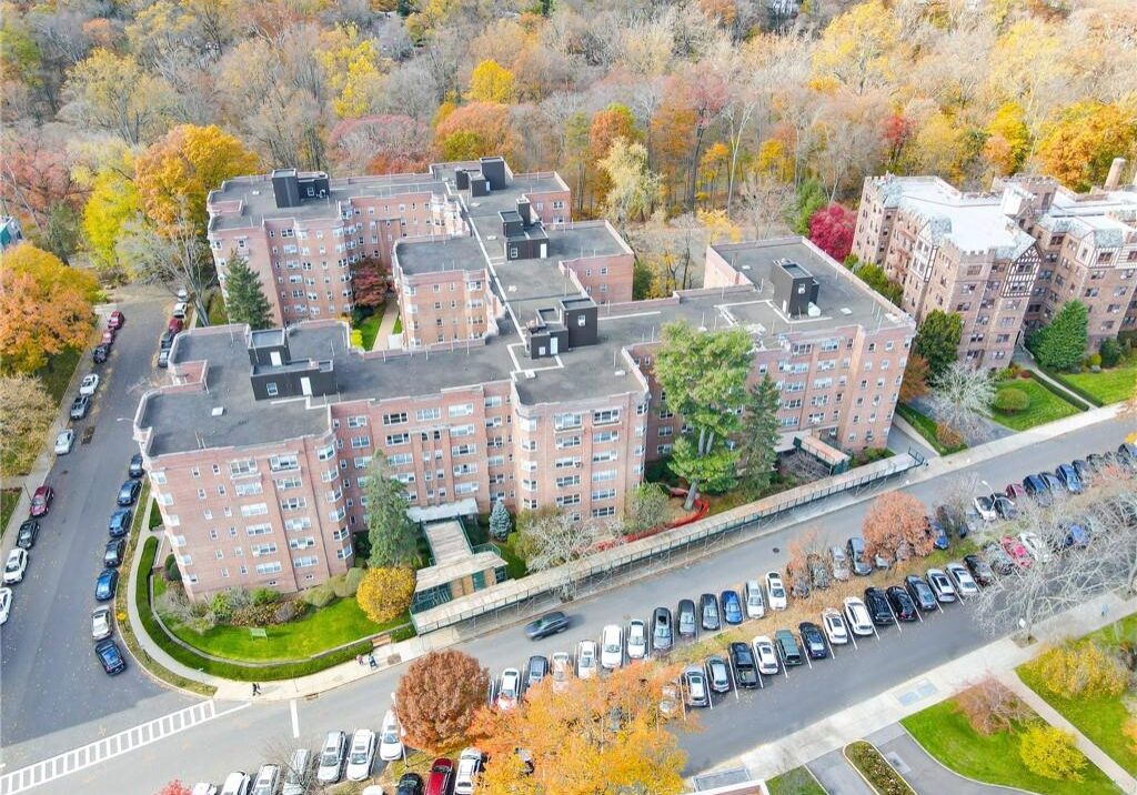 Aerial view of a residential complex surrounded by autumn trees and parked cars.