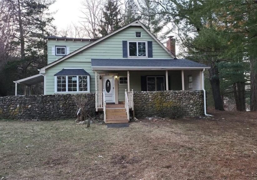 A two-story house with a stone porch and light blue siding.