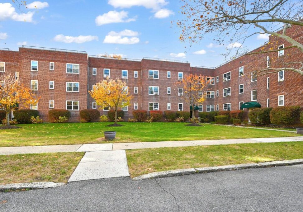 Brick apartment building with a green lawn and autumn trees.