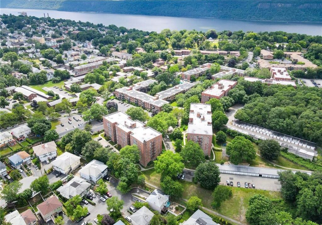 Aerial view of a riverfront town with residential buildings and greenery.