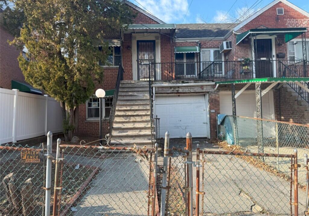 Old brick house with stairs and gated driveway in an urban setting.