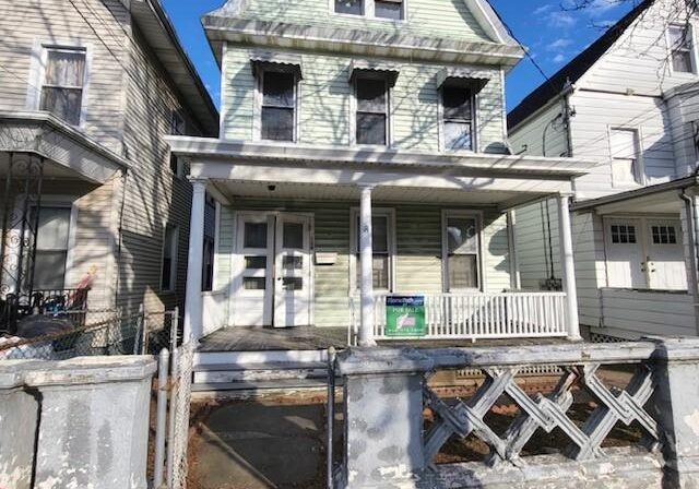 A weathered, three-story house with a porch and peeling paint under a clear blue sky.
