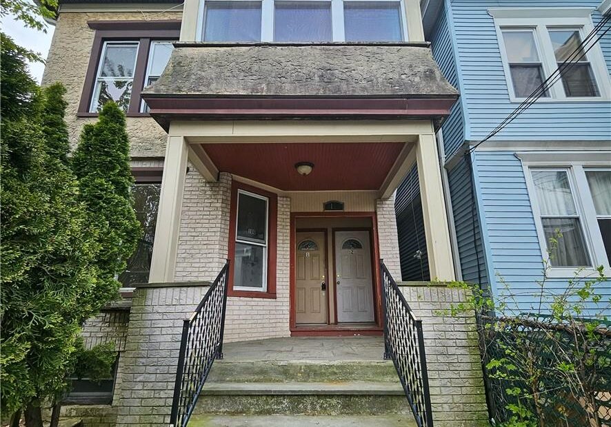 Front view of a stone and wood townhouse with stairs and iron railings.