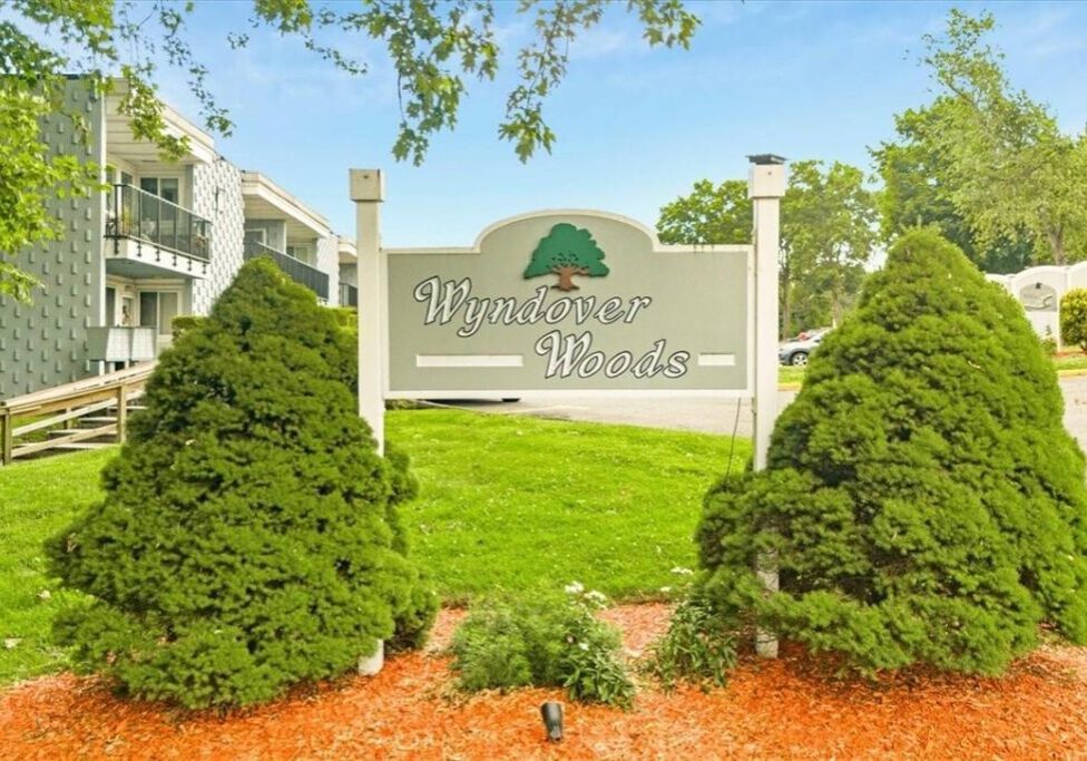 Welcome sign for Whispering Winds community surrounded by greenery.